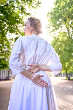 Şık, orta yaşlı, beyaz bir elbise giymiş, güneşli bir sokakta.                      