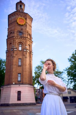 Vinnytsia 'daki tarihi su kulesinin yanındaki meydanda beyaz bir elbise giymiş şık bir genç kadın.                  