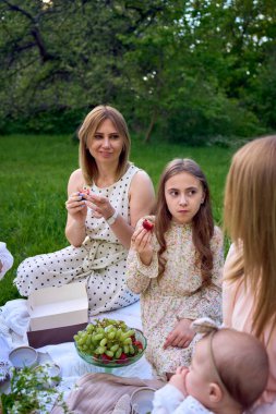 İki kadın ve çocukları bahçede piknik yapıyorlar.