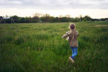 Oyuncak tavşanlı güzel sarışın kız tarlada oynuyor.