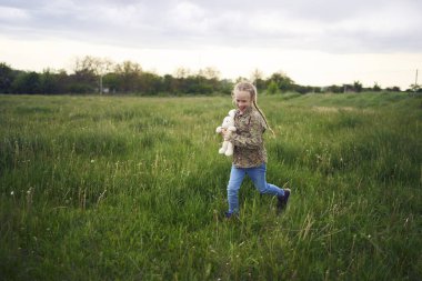 Oyuncak tavşanlı güzel sarışın kız tarlada oynuyor.