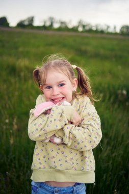 Oyuncak tavşanlı güzel sarışın kız tarlada oynuyor.
