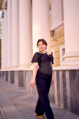 Antika sütunları olan bir tiyatronun yanında siyah korseli orta boylu bir kadın.                      