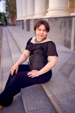 Antika sütunları olan bir tiyatronun yanında siyah korseli orta boylu bir kadın.                      