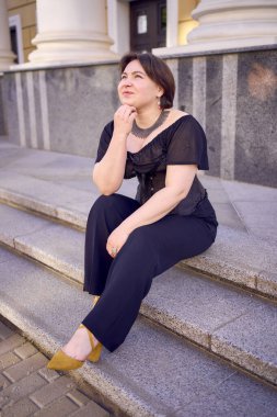 Antika sütunları olan bir tiyatronun yanında siyah korseli orta boylu bir kadın.                      