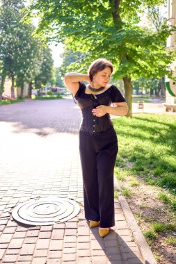  Orta boylu, siyah korseli ve geniş paçalı bir kadın sabah vakti şehirde yürür.                            