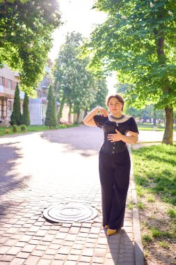  Orta boylu, siyah korseli ve geniş paçalı bir kadın sabah vakti şehirde yürür.                            