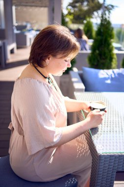  Orta boylu, şeftali tüyü elbiseli bir kadın. Sabah vakti kahve dükkanında kahve içiyor.               