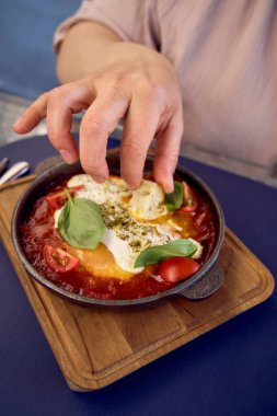 Orta boylu, şeftali tüylü bir kadın modern restoranda Shakshouka yiyor.