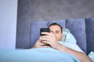 Genç adam sabah uyandıktan sonra akıllı telefondan kayar, sabah rutini.