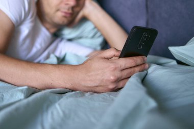young man scrolls in smartphone in the morning after waking up, morning routine clipart