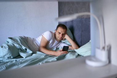 Genç adam sabah uyandıktan sonra akıllı telefondan kayar, sabah rutini.