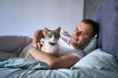  Genç adam yatakta kedi besliyor, sabah rutini.                              