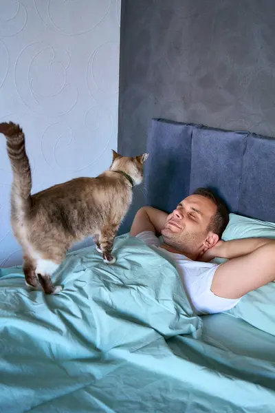 Genç adam göğsünde bir kediyle uyuyor, sabah rutini.