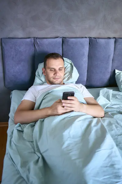 stock image young man scrolls in smartphone in the morning after waking up, morning routine