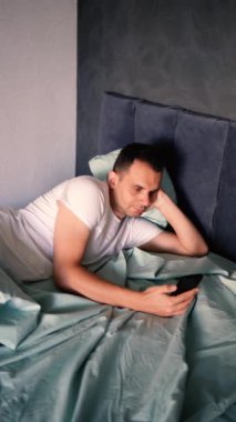 Genç adam sabah uyandıktan sonra akıllı telefondan kayar, sabah rutini.