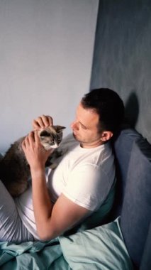 Genç adam yatakta kedi besliyor, sabah rutini.