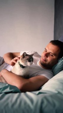 Genç adam yatakta kedi besliyor, sabah rutini.