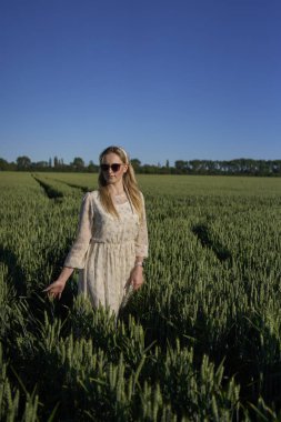 Yeşil buğday tarlasında pastel şifonlu bir elbise giyen sarışın bir kadının portresi.