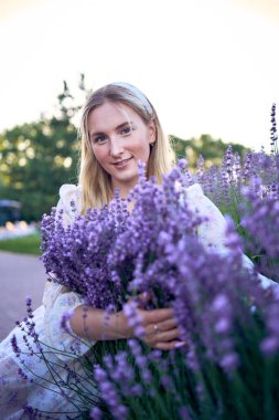 Lavanta çalıları arasında pastel şifon bir elbise içinde genç sarışın bir kadının portresi.