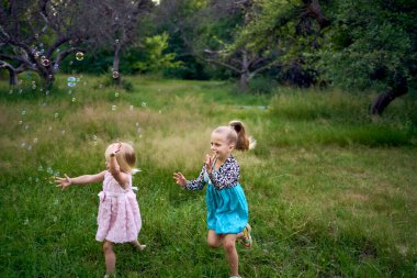 çocuk ve bebek, kız kardeşler, bahçede kabarcıklar yakalıyorlar.