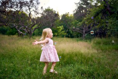  Pembe bulutlu bir bebek bahçede sabun köpüğü yakalar.                  