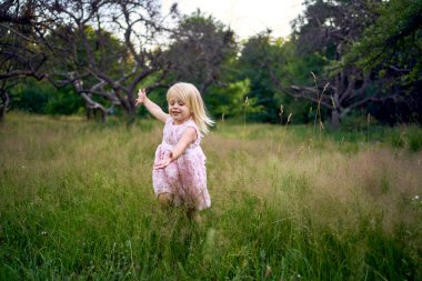 Pembe bulutlu bir bebek bahçede bir uçak gibi koşuyor.