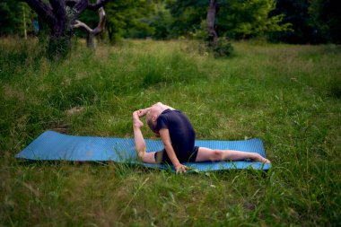 Siyah minimalist tulumlu 5 yaşındaki küçük bir kız bahçede jimnastik yapıyor.
