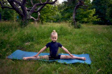 Siyah minimalist tulumlu 5 yaşındaki küçük bir kız bahçede jimnastik yapıyor.