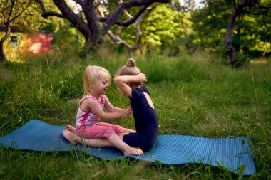 Siyah minimalist tulumlu 5 yaşındaki jimnastikçi, yürümeye yeni başlayan kız kardeşinin egzersizlerini gösteriyor.
