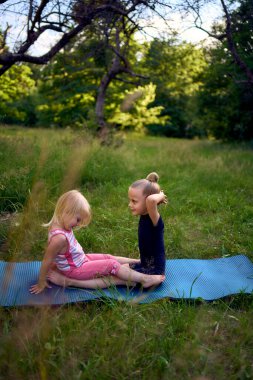Siyah minimalist tulumlu 5 yaşındaki jimnastikçi, yürümeye yeni başlayan kız kardeşinin egzersizlerini gösteriyor.