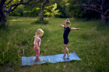 Siyah minimalist tulumlu 5 yaşındaki jimnastikçi, yürümeye yeni başlayan kız kardeşinin egzersizlerini gösteriyor.