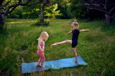 Siyah minimalist tulumlu 5 yaşındaki jimnastikçi, yürümeye yeni başlayan kız kardeşinin egzersizlerini gösteriyor.