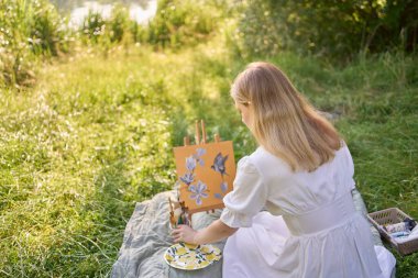  Beyaz elbiseli güzel genç bir sanatçı nehir kıyısına bir resim çiziyor.