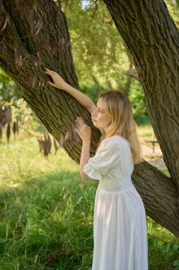 Nehir kıyısındaki ağaçların arasında beyaz elbiseli güzel bir sanatçı.