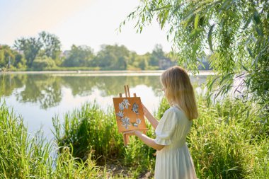 Nehir kıyısındaki ağaçların arasında beyaz elbiseli güzel bir sanatçı.