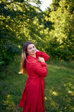 Parktaki kırmızı elbiseli, uzun sarı saçlı, 30 yaşında güzel bir kadının portresi.