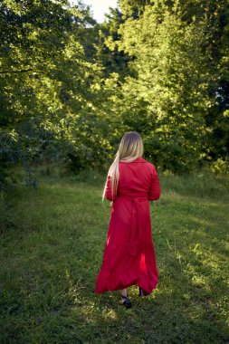 Parktaki kırmızı elbiseli, uzun sarı saçlı, 30 yaşında güzel bir kadının portresi.