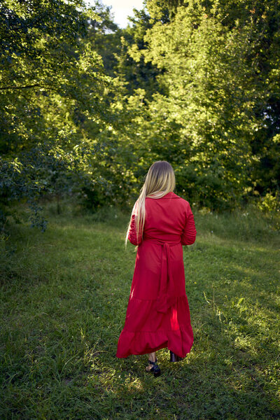 портрет красивой 30-летней женщины с длинными светлыми волосами в красном платье в парке