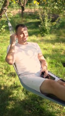 Bir adam dinlenir ve hamakta müzik dinler, köpeği yakınlarda dinlenir.