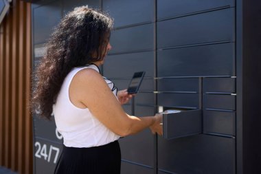     Kadın mobil uygulama kullanarak bir posta terminalinden bir paket alıyor.                           