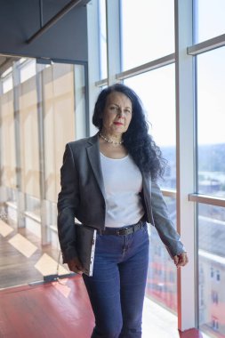         57 yaşında bir kadın, modern çalışma alanındaki cam ofisine dizüstü bilgisayarla gidiyor.                       