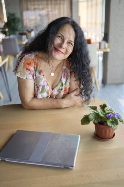 57 yaşındaki bir kadın, modern bir ofis çalışma alanında dizüstü bilgisayarda çalışıyor.                    