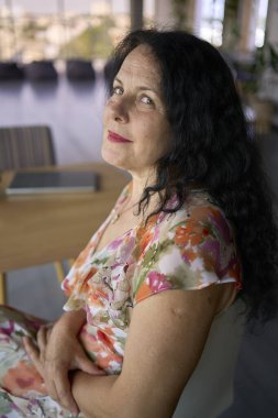 57 yaşındaki bir kadın, modern bir ofis çalışma alanında dizüstü bilgisayarda çalışıyor.                    