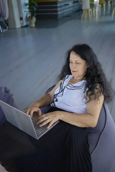 stock image a  57-year-old woman works on a laptop in a modern office workspace  sitting in a beanbag chair                  