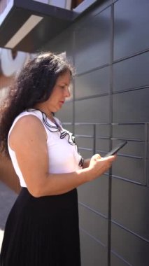 Bir kadın mobil uygulama kullanan bir posta terminalinden cep telefonu uygulaması kullanarak bir paket alıyor.