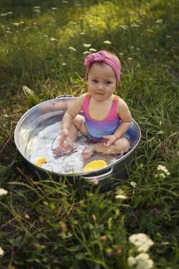 Metal bir küvette bir bebek yaz bahçesinde plastik ördek yavrularıyla oynuyor.