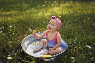 Metal bir küvette bir bebek yaz bahçesinde plastik ördek yavrularıyla oynuyor.