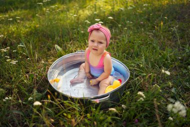 Metal bir küvette bir bebek yaz bahçesinde plastik ördek yavrularıyla oynuyor.