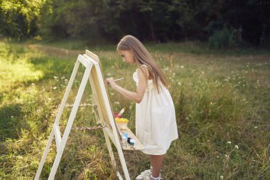 Yazlık elbiseli bir genç kız bahçeye resim çiziyor.